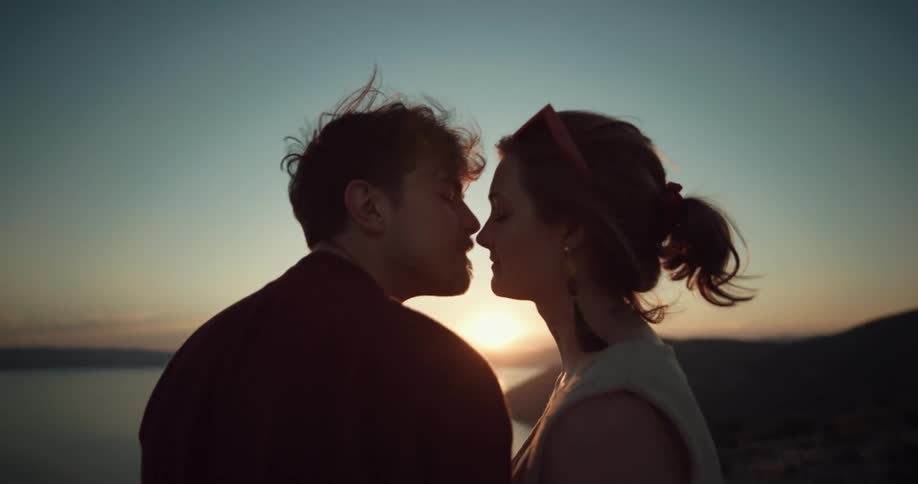 A man and woman kiss and laugh together overlooking the coast at sunset