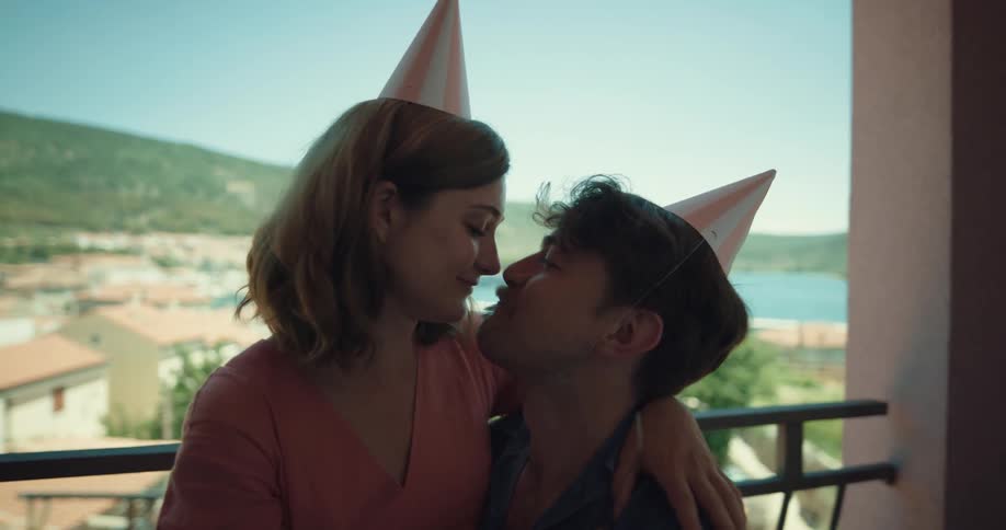 A woman sits on a mans lap and feeds him cake as they laugh and kiss