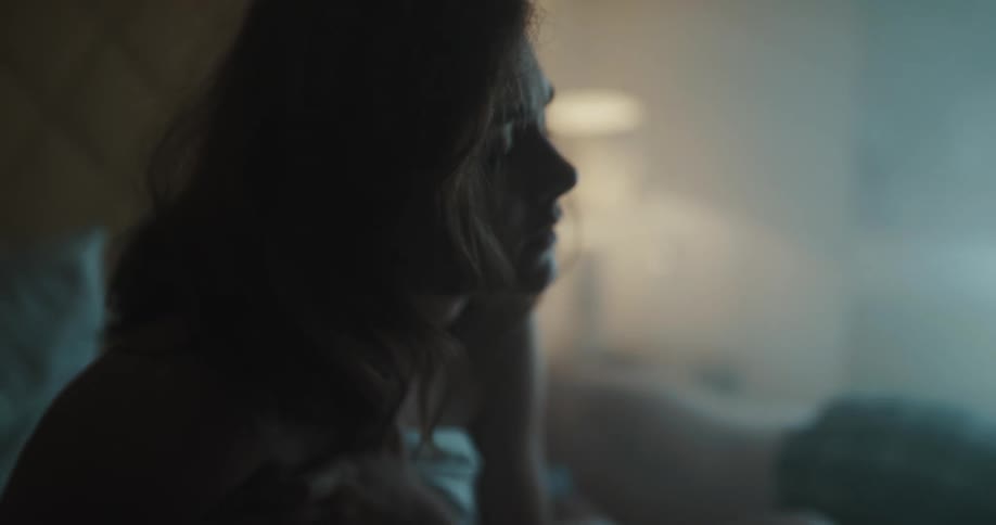A woman looks sad as she sits up in bed while a man sleeps