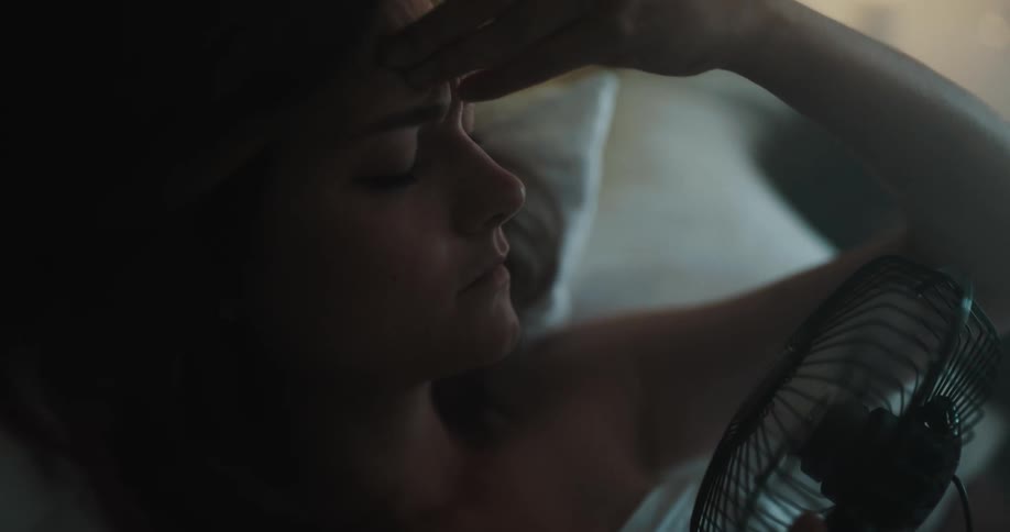 A woman is laying in bed and holding a fan