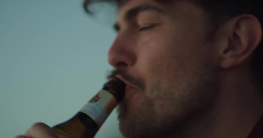 Man playfully blowing on beer bottles before drinking from them