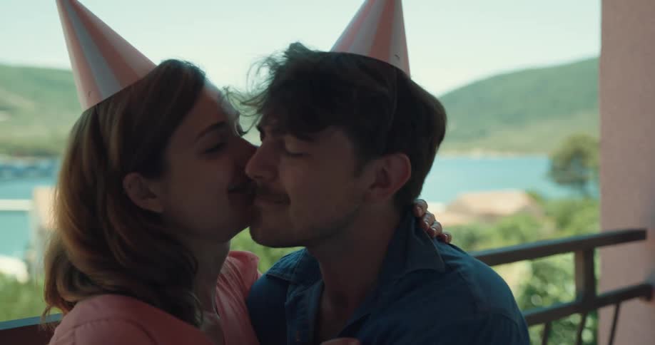 A man and woman kiss and snuggle sitting on a balcony with a beautiful lake in the background
