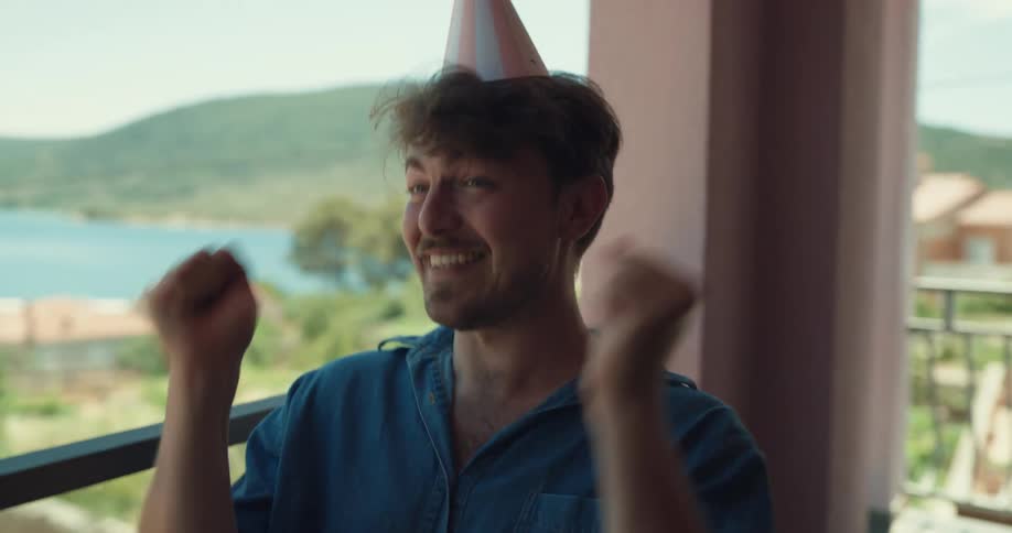 Couple celebrates mans birthday with cake sitting on balcony overlooking town sitting on shore of lake near hills