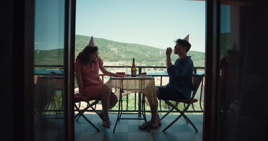 Young couple wearing party hats celebrate drinking wine in the balcony at home