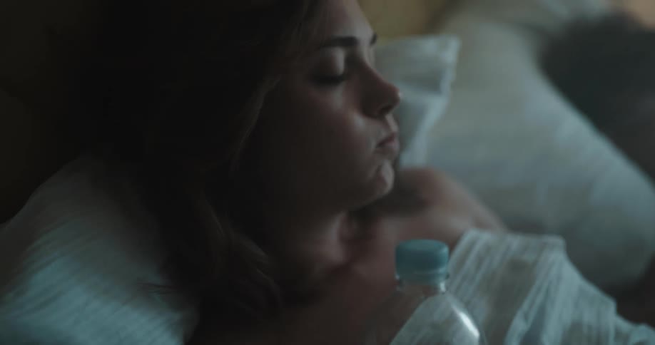 Woman laying in a hot day uses a portable fan and drinks water from a plastic bottle