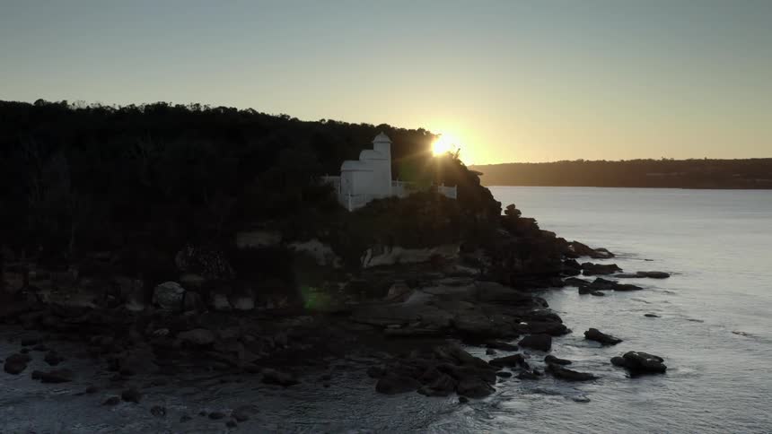 Ocean waves roll into the rocks near the hill as the sun rises