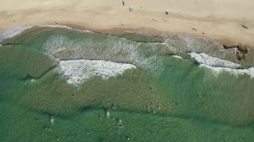 Aerial view of a beach next to the ocean with people swimming