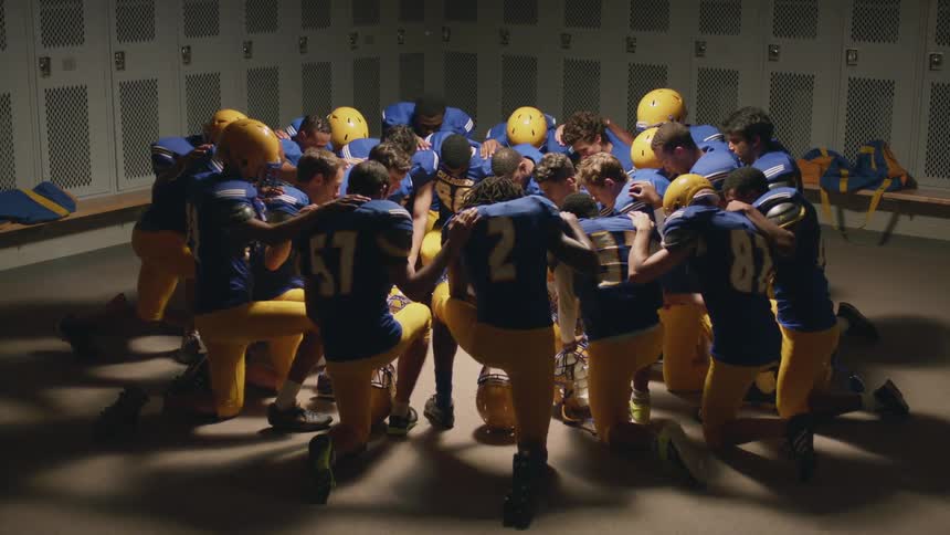 A football team gathers in the locker room praying