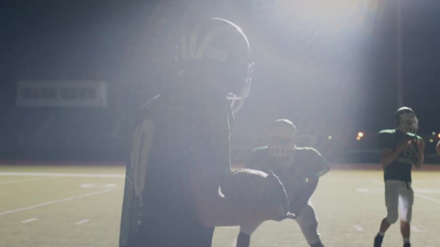 A football player walks up with the ball to some other players in a stadium