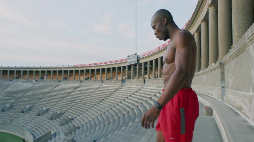 A man in running shorts and no shirt runs up stairs in a stadium