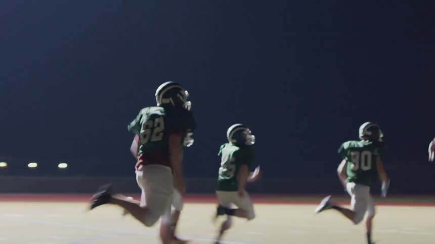 Football players racing down a long field at night