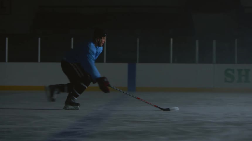 A hockey player is racing down the ice hitting hockey pucks in a dark area