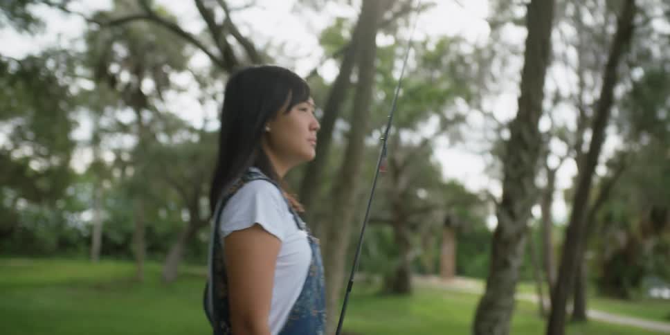 A woman is walking outdoors with a fishing pole