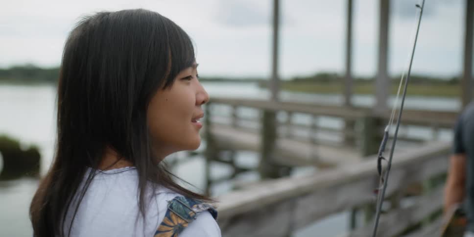 A woman carrying a fishing rod walks behind a man on a dock
