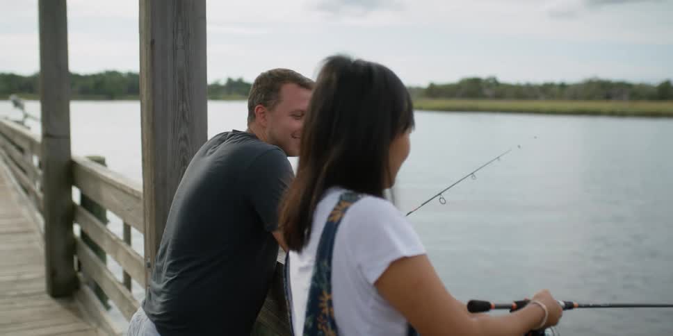 A man and woman lean against a dock railing fishing and smiling at each other