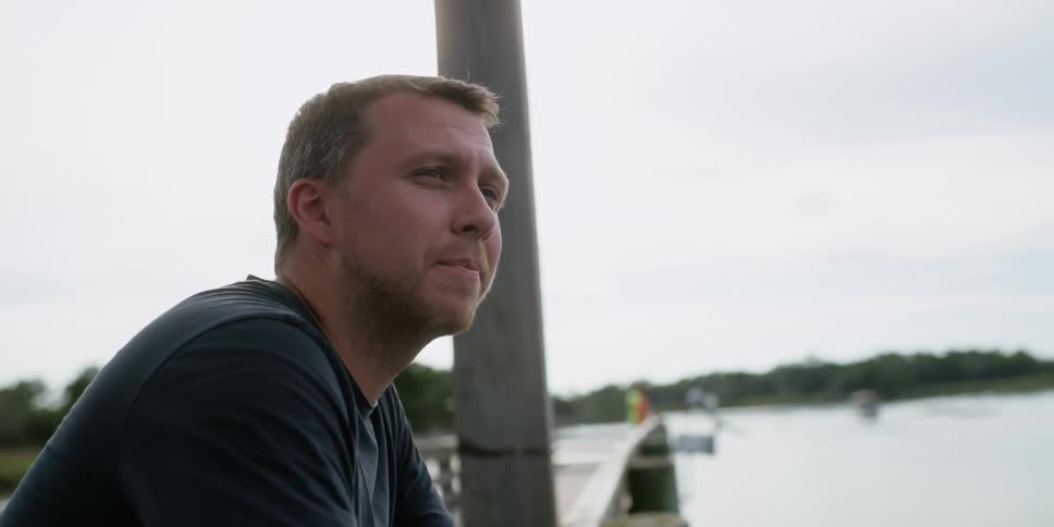 A man gazes out at his surroundings while relaxing on a pier on a lake on a cloudy day