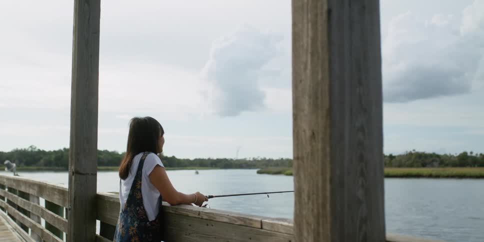 A woman leaning against the pier railing and fishing