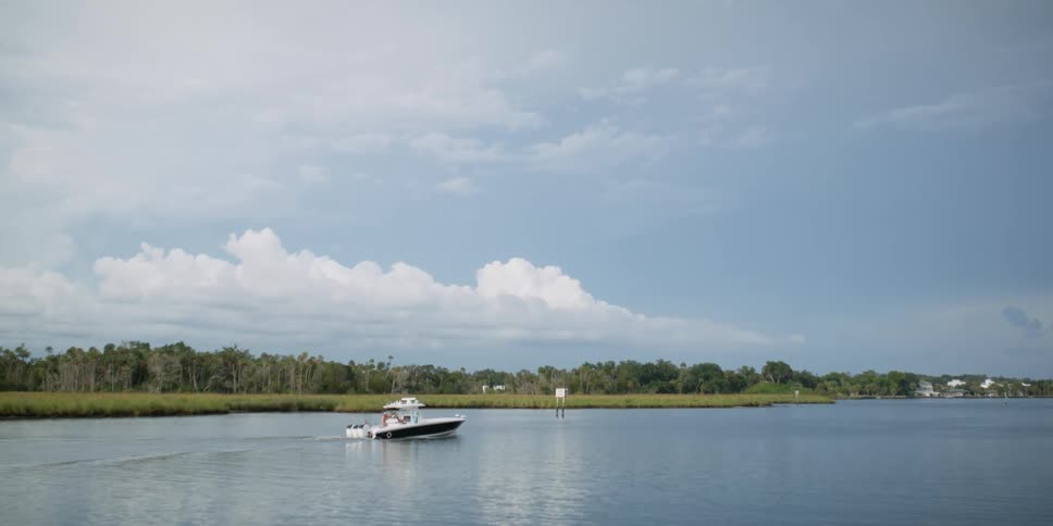 Small boat leisurely moving over the surface of a lake under a blue sky