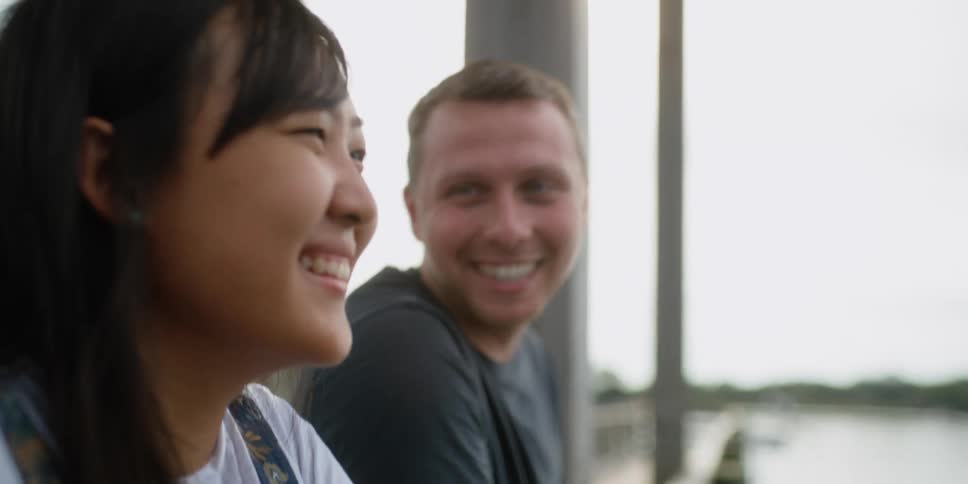 Man and woman smile and laugh as they stand near a lake