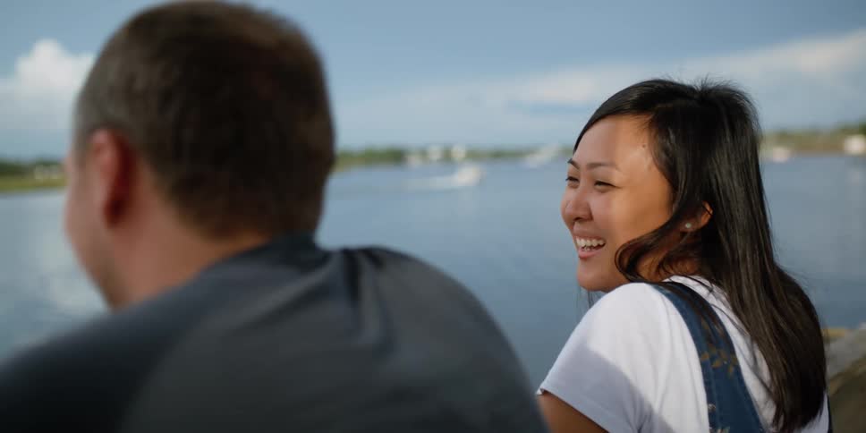 A man and a woman talk and laugh with one another near a body of water