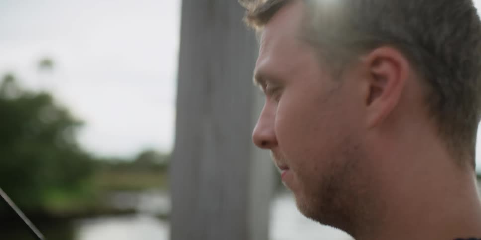 A man fishes off a dock near palm trees