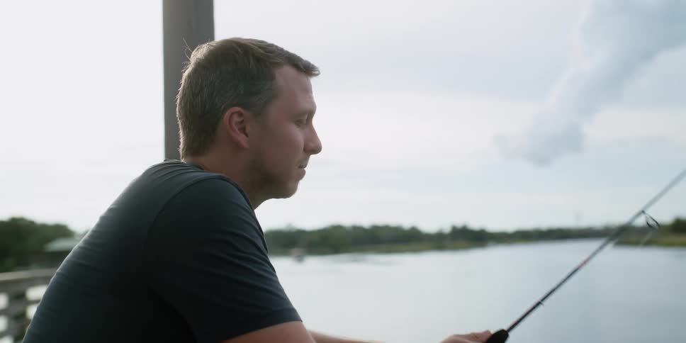 A man leans over the railing at a dock while holding onto his fishing rod