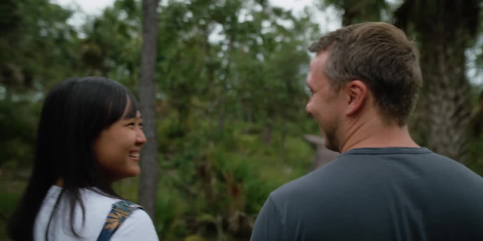 Man and woman look and talk to on another affectionately walking among palm trees