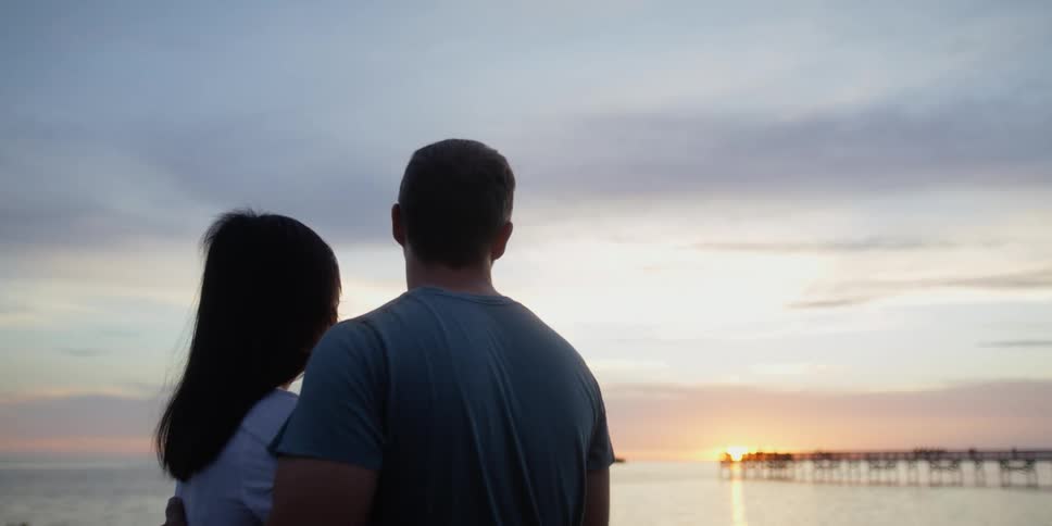 Husband and wife are watching the sunset together by the beach