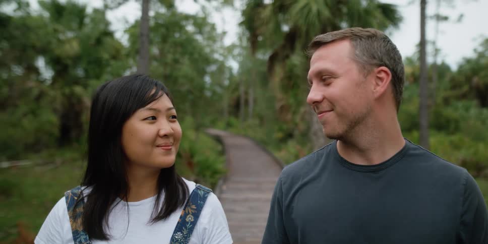 A man and woman stand outdoors while smiling and looking at each other