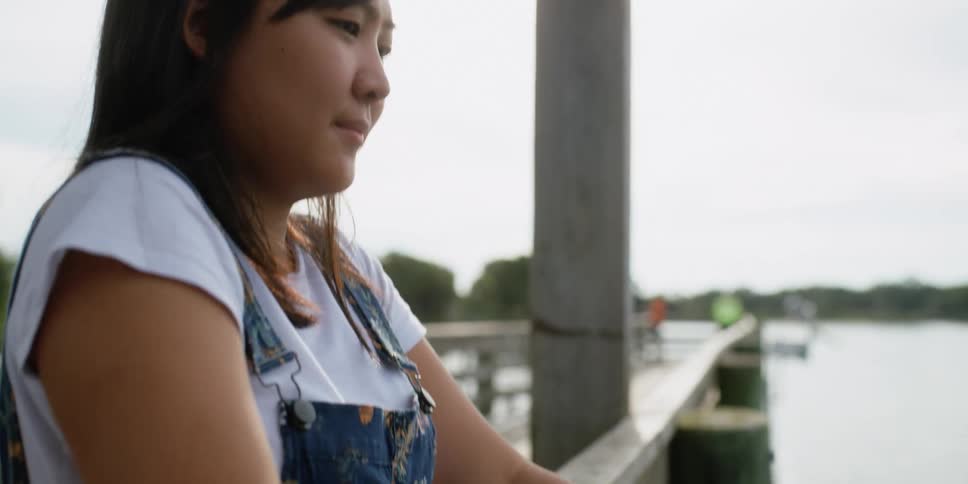 A woman flicks her fishing rod to cast her fishing line as she stands on a wooden dock