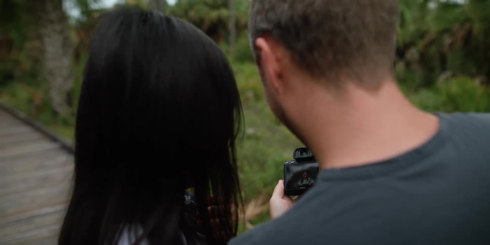 A man and woman are outdoors and looking at a camera