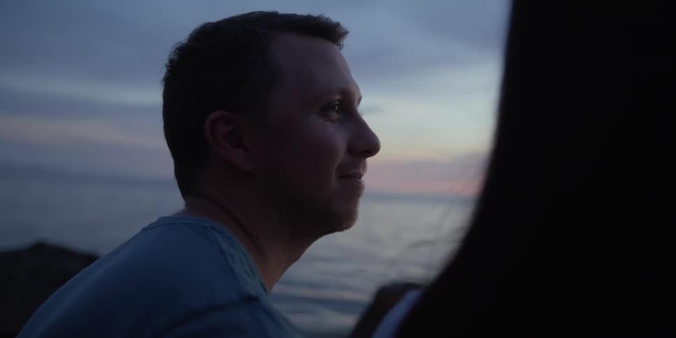 Man and woman sit on a wall at seaside at dusk
