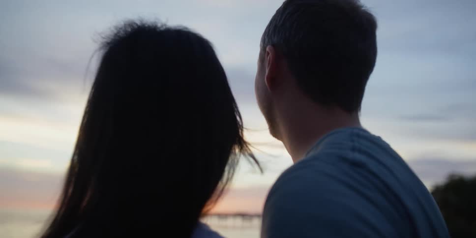 A man places his arm around his girlfriend as they turn to look at a lake