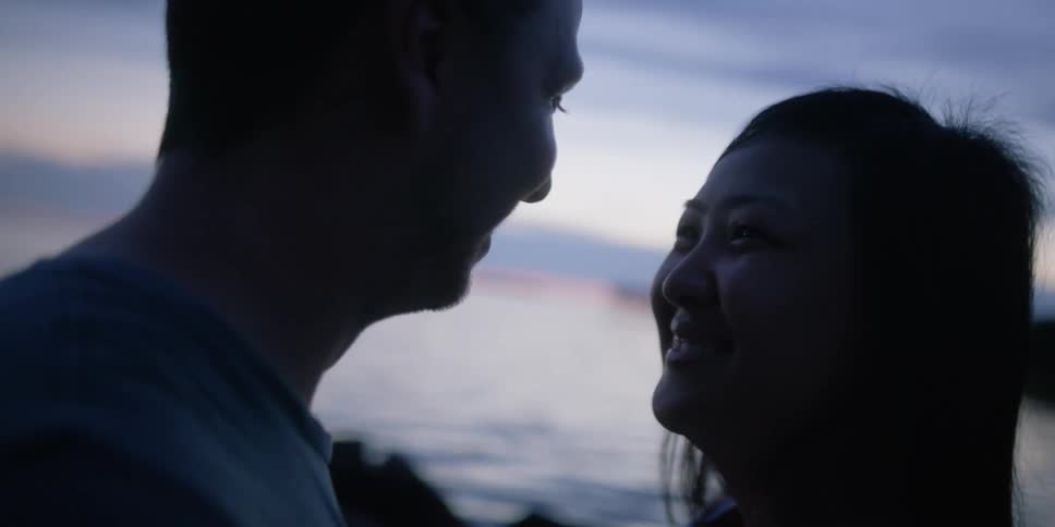 Woman caresses mans face as they look at each other lovingly while standing near a lake