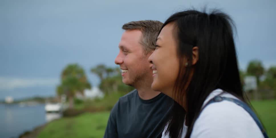 A man and woman stand on the shore and laugh as they look towards the water