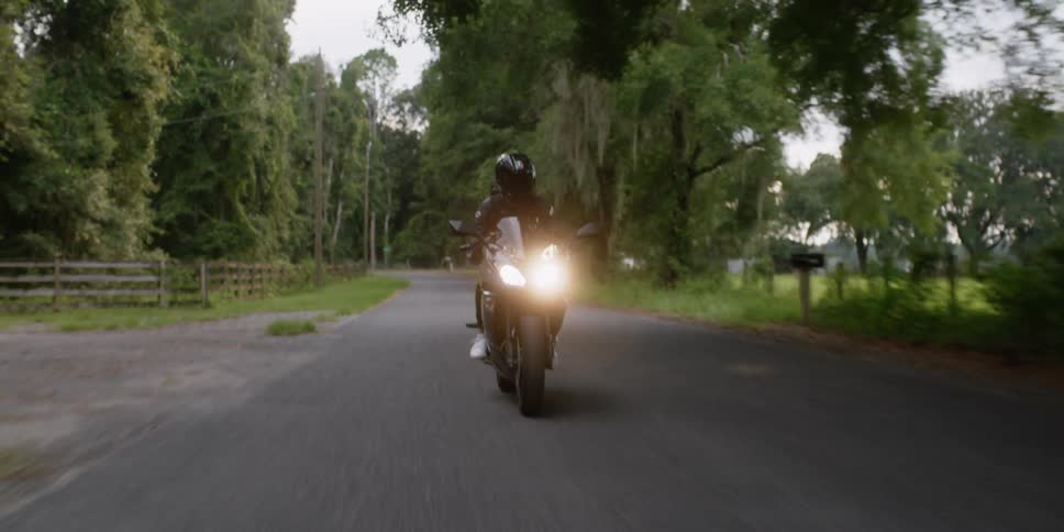 Cyclist wearing a black jacket and black helmet is riding a motorcycle with the headlights on