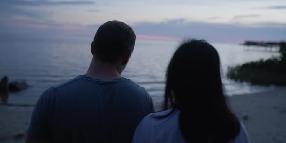 A man and woman are walking on the beach at dusk