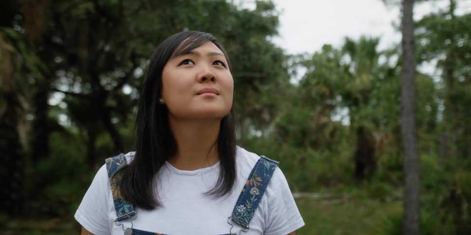 A woman is standing outdoors in a wooded area in spring