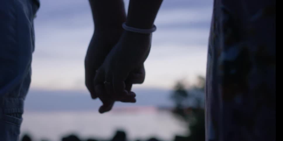 Man and woman holding hands walk down the road and are silhouetted against the sky at dusk