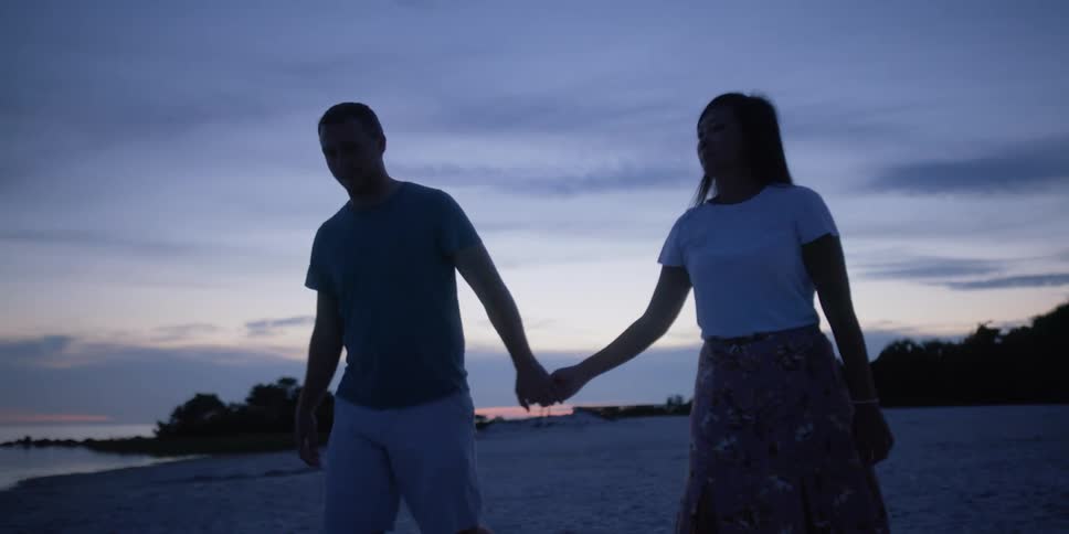 A man and woman walk along the beach holding hands