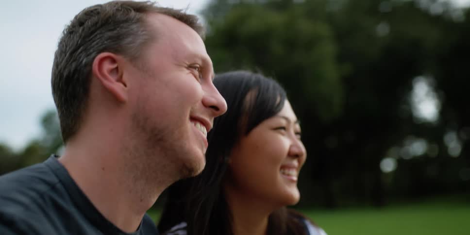 A couple laugh and smile at each other as they relax in a park