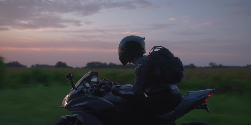 A motorcyclist rides down a road through the countryside in the evening