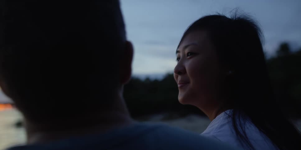A man and woman sitting on a beach at dusk