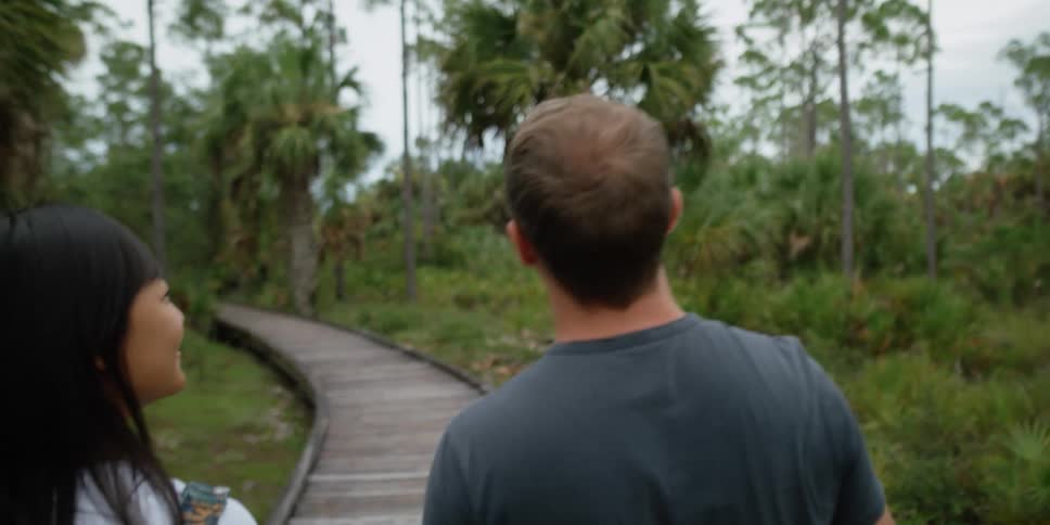 A man and woman walking outdoors in a forest area
