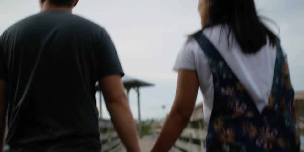 A man and woman hold hands walking to the end of a pier