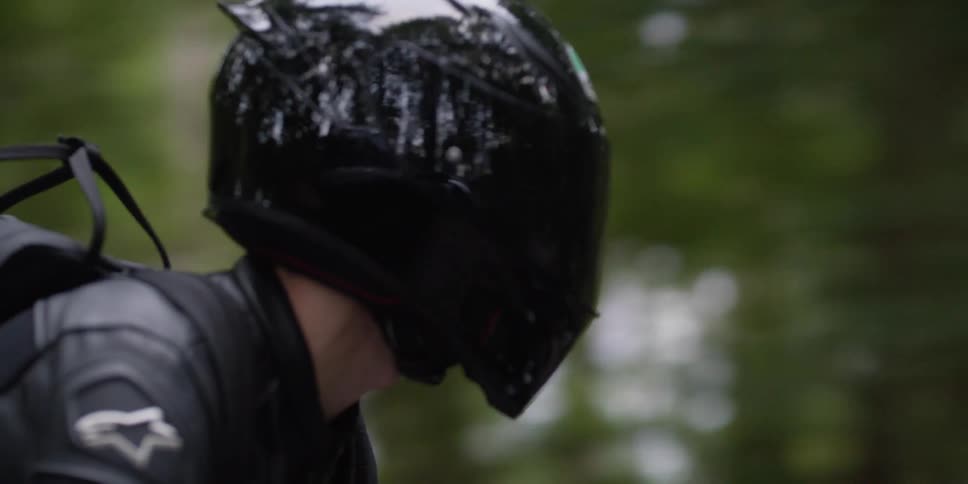 A motorcyclist dressed in all black rides past trees in a forest