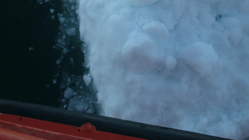 A red boat floats by a chunk of snowy ice