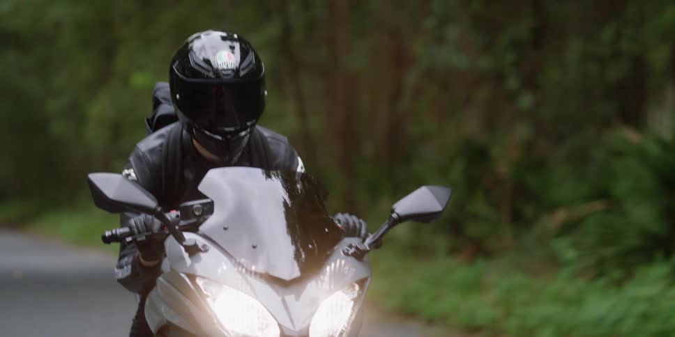A person driving a motorcycle wearing black leather jacket and crash helmet