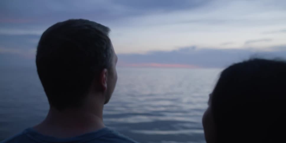 A man and woman look out at the water as they talk