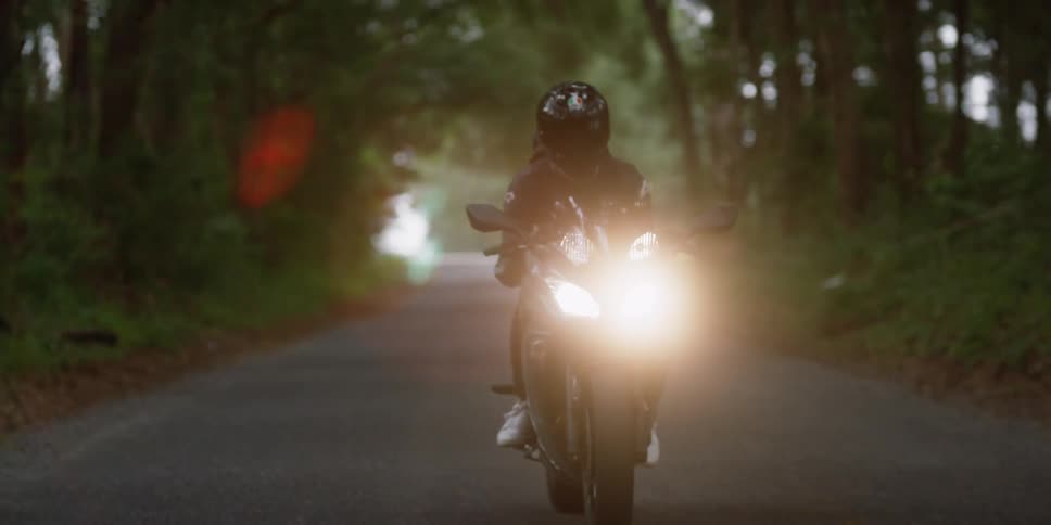Cyclist wearing a black jacket and black helmet is riding a motorcycle with the headlights on